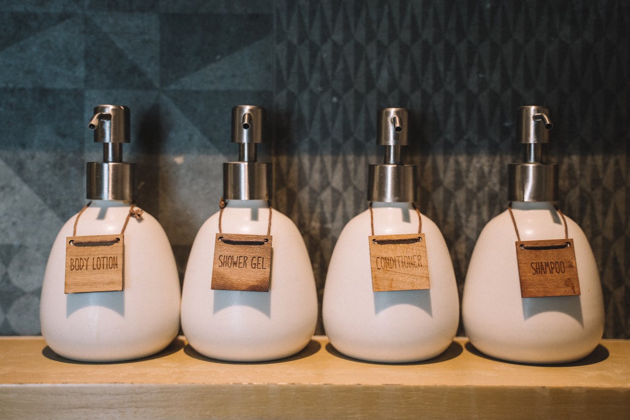 Elegant pump bottles holding bath essentials like lotion, gel, and more on a wooden shelf.